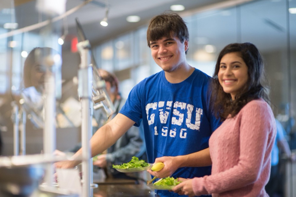 Two students making a salad and smiling at the camera.
